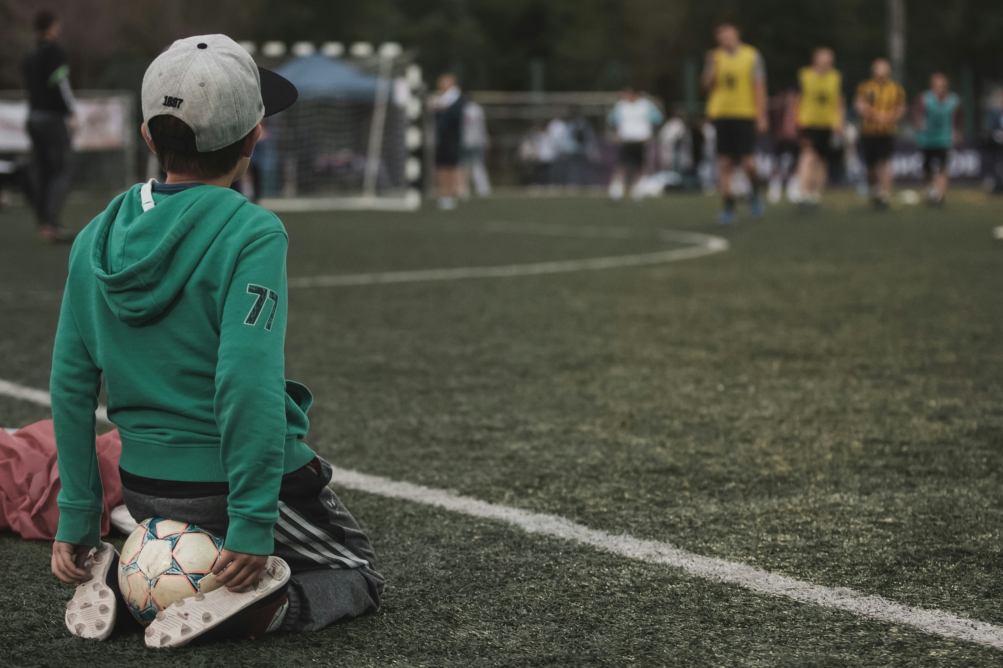 man in green and white long sleeve shirt and black pants sitting on green grass field